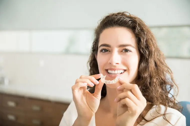 Mujer joven sosteniendo un alineador transparente de Invisalign